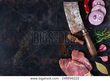 Raw Pork Chops And Meat Cleaver On Dark Background. Top View With Copy Space
