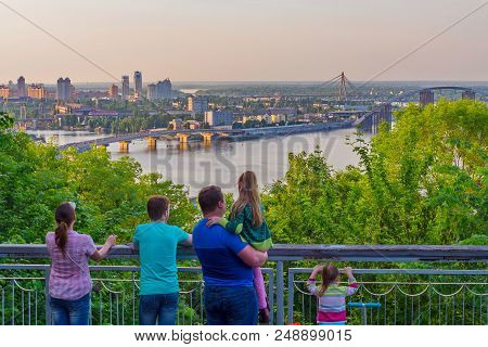 The Family Looks At The Panorama Of The City With Three Bridges Over The Dnieper Among The Lush Gree
