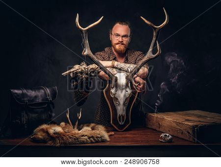 Redhead Taxidermist Hipster Male In Sunglasses Dressed In A Brown Shirt, Standing Near A Table With 
