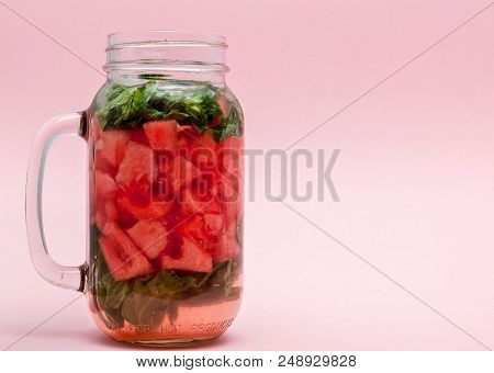 Jar Of Cold Fresh Lemonade With Piece Of Watermelon And Ice On Pink Background.