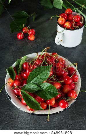 Full Bowl And Mug Of Pink Cherries With Leaves, On Dark Surface