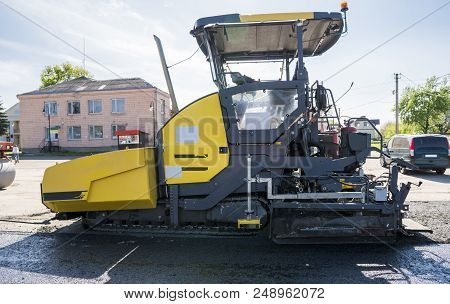 Worker Operating Asphalt Paver Machine During Road Construction And Repairing Works. A Paver Finishe