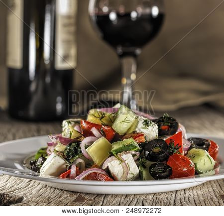 Greek Salad And Glass Of Red Wine On Wooden Table, Feta Cheese, Tomatoes, Red Onion, Cucumber, Lettu