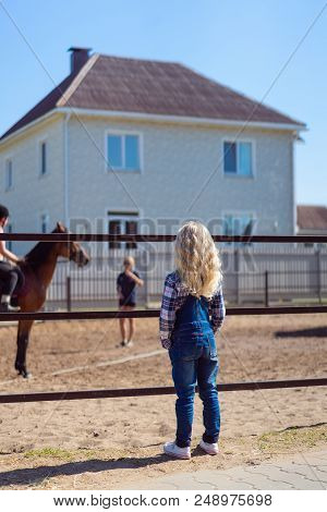 Rear View Of Child Looking At Mother Riding Horse At Ranch