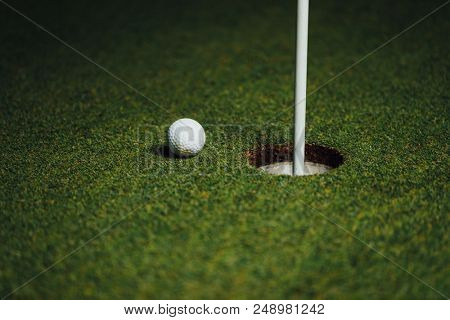 golf ball nearby hole with pin flag, green grass background, closeup view