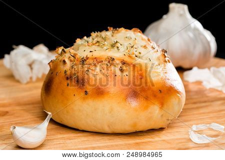 Close-up Of Homemade Mini Pizza Bun Topped With Cheese, Garlic And Herbs On Round Wooden Board On Da
