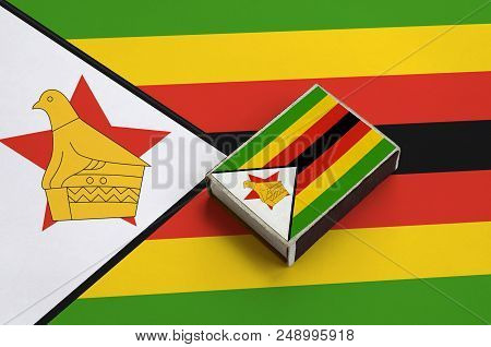 Zimbabwe Flag  Is Pictured On A Matchbox That Lies On A Large Flag.