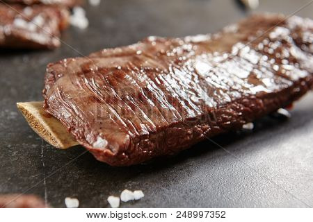 Hot Grilled Whole Flank Steak on Black Stone Background. Fresh Juicy Medium Rare Beef Grillsteak. Barbecue Meat Close Up