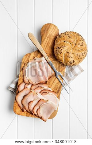 Sliced smoked ham. Tasty pork meat and bun on wooden cutting board. Top view.