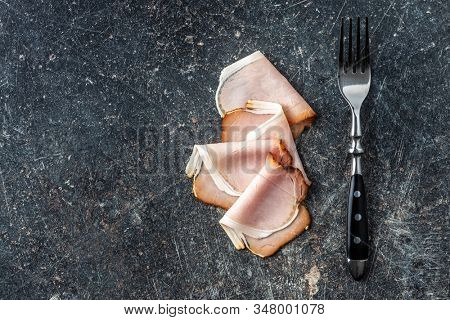 Sliced smoked ham. Tasty pork meat and fork on old kitchen table. Top view.