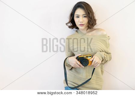 Portrait Of Beautiful Young Asian Woman Holding Instant Camera And Looking At Camera On Beige Backgr