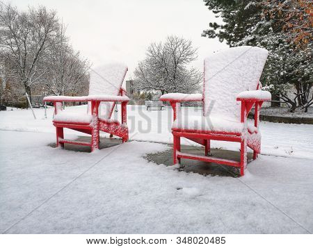 Two Red Wooden Adirondack Muskoka Chairs Covered With Snow On Winter Day In Park Outdoor. Winter Sea