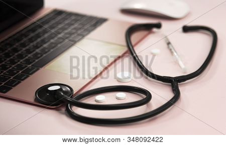 Doctors Desk With Stethoscope Keyboard Notepad And Pen, Prescription And Pills On Pinck Background