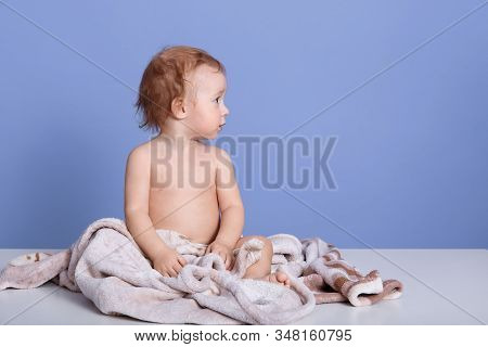 Close Up Portrait Of Baby Boy Sitting On Towel, Posing Bared Isolated Over Blue Studio Background, A