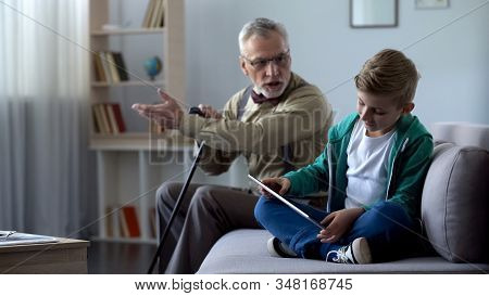 Angry Grandfather Scolding Boy For Playing Video Game On Tablet, Generation Gap