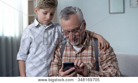 Boy Helping Grandfather To Better Understand Smartphone, Digital Generation Gap