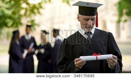 Senior Man In Academic Regalia Holding Diploma, Education At Any Age, New Degree