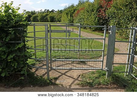 Galvanised Metal Kissing Gate At Park Entrance With A Limestone Chippings Path, And A Grass Meadow A