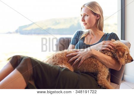 Woman Relaxing In Chair By Window At Home With Pet Dog