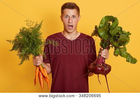 Horizontalshot Of Young Man With Vegetables In Front Of Him In Both Hands, Posing Isolated Over Yell