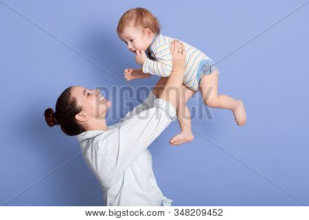 Side View Of Mid Adult Caucasian Mom Lifting Happy Toddler Son Into Air Above Head, Attarctive Mommy