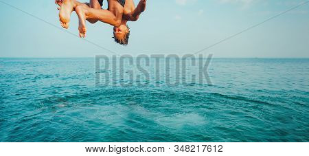 Young Man Jumping Off Cliff Into Blue Water Ocean At Sunset. Active Outdoor, Holiday Adventure, Tour