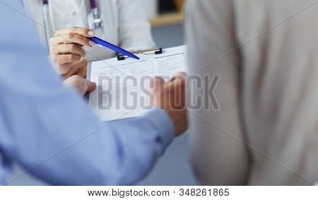 Doctor And Patient Examining A File With Medical Records, She Is Sitting On A Wheelchair