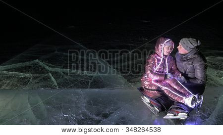 Young Loving Couple Skating At Ice Rink At Night. Man And Woman Kiss Hug Have Fun Learn To Skate. Ma
