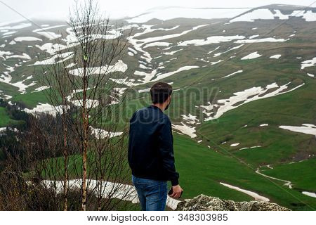 Back View Of A Male Tourist Who Travel In Mountains With Green Landscape Of High Tableland With Rest