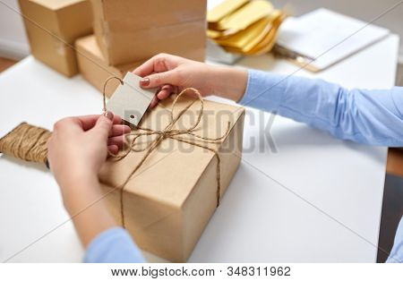 delivery, mail service, people and shipment concept - close up of female hands tying name tag to parcel box at post office