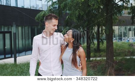Multiethnic Couple In Love Shyly Looking At Each Other, Talking And Walking Down The Street. He Kiss