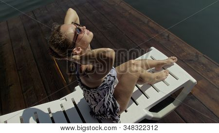 Woman Lie On A Sunbed In Sunglasses And A Boho Silk Shawl. Girl Rest On A Flood Wood Underwater Pier