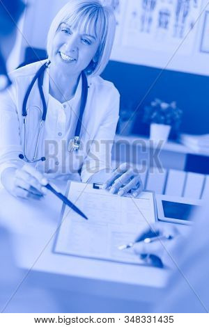 Doctor and patient examining a file with medical records, she is sitting on a wheelchair