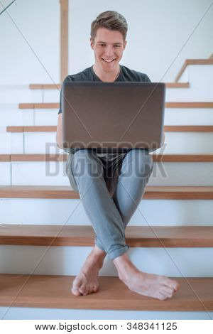 smiling young man in home clothes uses laptop