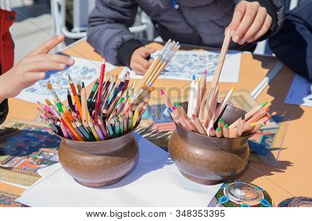The Boy Picks Up A Copper Bowl. View Of A Set Of Colored Pencils . Colored Pencils On The White Back