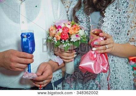 Bride And Grooms Hands With Wedding Flowers . The Bride Holds The Blue In Her Hand, The Red Bakal In
