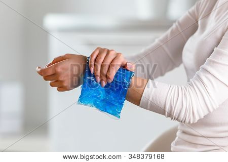 Woman Applying Cold Compress To A Her Painful Wrist Caused By Prolonged Work On The Computer, Laptop