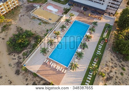 Top Down Aerial View Of Hotel Swimming Pool With Crystal Blue Water Surrounded With Palm Trees And D