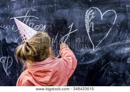 Girl In A Holiday Cap Draws A Heart With Chalk. Valentine Day Concept.