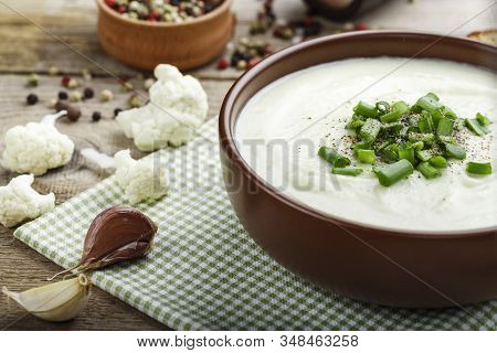 White Vegetable Cream Soup Of Cauliflower In A Brown Clay Plate On A Wooden Background. Simple Diet 
