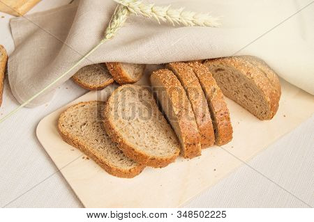 Sliced Slices Of Coarse Rye Bread On A Wooden Cutting Board With A Linen Cloth And Rye Ears, The Con