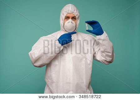 A Male Doctor In Protective Overalls And A Mask Pointing At Ampoule With A Vaccine In His Hands. Cor