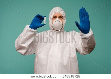 A Male Doctor In Protective Overalls And A Mask Holds An Ampoule With A Vaccine In His Hands Shows S