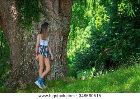 Teenager Stands Looking To Side While Leaning Against Large Tree In Natural Park Of Mclaren Falls Pa