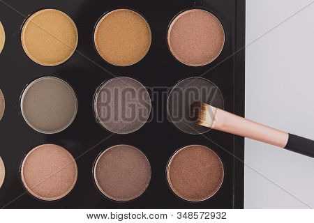 Close-up Of Brush On Top Of Eyeshadow Palette With Trendy Nudes And Bronzy Tones