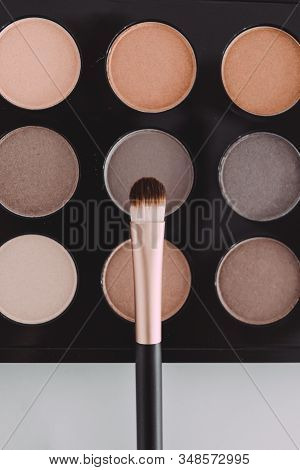 Close-up Of Brush On Top Of Eyeshadow Palette With Trendy Nudes And Bronzy Tones