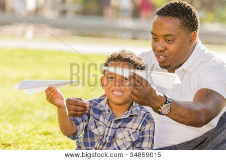 Feliz African American pai e filho de raça mista brincando com aviões de papel no Parque.