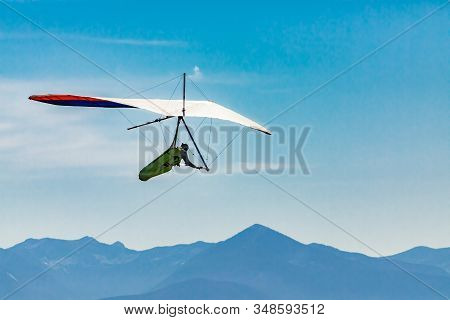 Flying Hang Glider Man In Action. Beautiful Mountains View In The Background. Extreme Leisure Activi