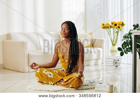 Smiling Calm Young Woman Meditating At Home In Lotus Position