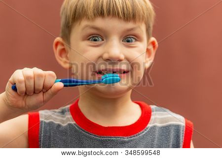 The Child Holds A Toothbrush In His Hand Near His Mouth